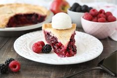 a piece of pie on a white plate with berries and ice cream in the background