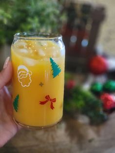 a person holding up a glass with orange juice in front of christmas decorations on the table