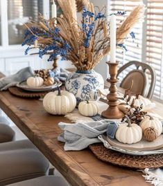 a wooden table topped with lots of white pumpkins and blue flowers on top of it