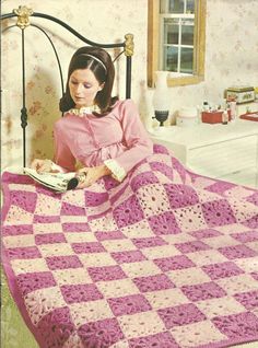 a woman sitting on top of a bed with a pink and white crocheted blanket