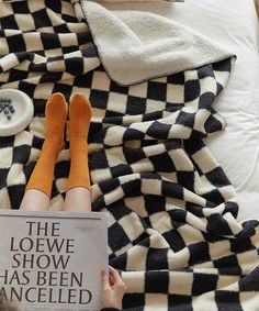 a person laying on a bed with their feet up and reading the book, the loewe show has been ancelled