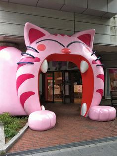 a large pink cat statue sitting on top of a brick floor next to a building