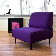 a purple chair sitting on top of a hard wood floor next to a black bird