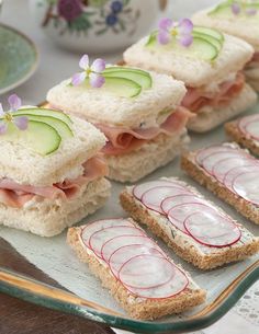 sandwiches with cucumber and ham are arranged on a plate next to a cup of tea