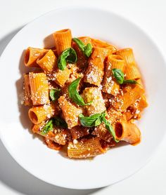 a white plate topped with pasta covered in sauce and basil sprinkled on top