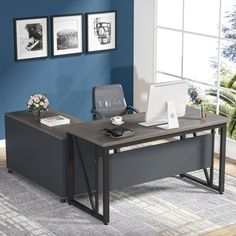 an office desk with a laptop on it in front of a blue wall and rug