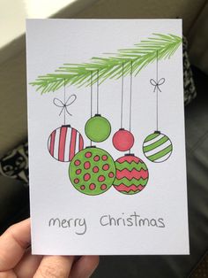 a hand holding up a christmas card with ornaments hanging from it