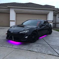 a black sports car parked in front of a house with purple lights on it's side