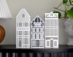 a white paper cut out of buildings on a table next to a lamp and vase