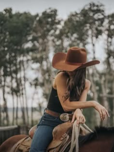 a woman riding on the back of a brown horse wearing a cowboy hat and jeans