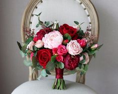 a bouquet of red and pink flowers sitting on top of a white chair in front of a mirror