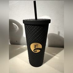 a black cup with a straw in it sitting on a white table next to a wall