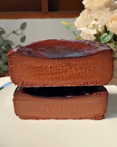 two pieces of chocolate cake sitting on top of a white plate next to a vase with flowers