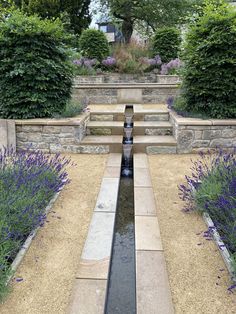 a water feature in the middle of a garden with lavenders and trees around it