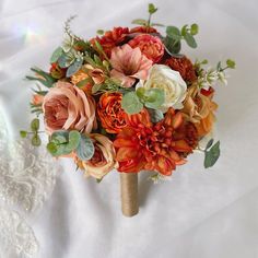 a bridal bouquet with orange and pink flowers on a white cloth covered bed sheet