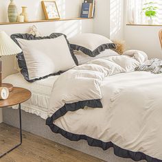 a bed with white sheets and black ruffles in a bedroom next to a window