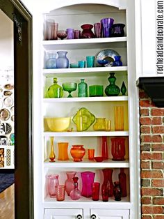 a white bookcase filled with lots of different colored glassware on top of it