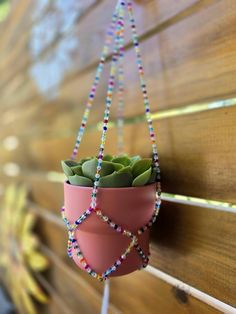 a pink potted plant hanging from a wooden bench with beads on the handle and string attached to it