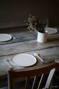 a wooden table topped with white plates next to a vase filled with flowers on top of it