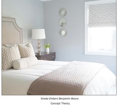 a bed with white sheets and pillows in a bedroom next to a window that has a fan on it