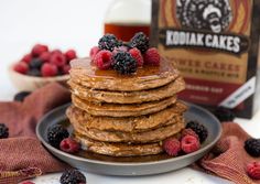 a stack of pancakes topped with berries and syrup next to a bottle of kodia cakes