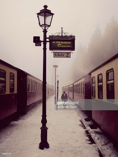 a train station with two trains parked on the tracks and people walking near by in the snow