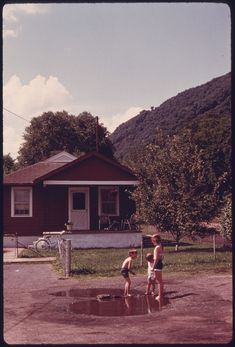 two young boys playing in a puddle on the side of a road next to a house