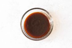 a glass jar filled with brown sauce on top of a white table