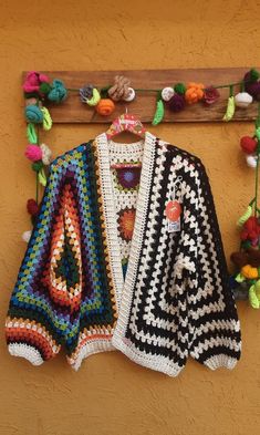 a crocheted jacket hanging on a wall next to a wooden hanger with flowers