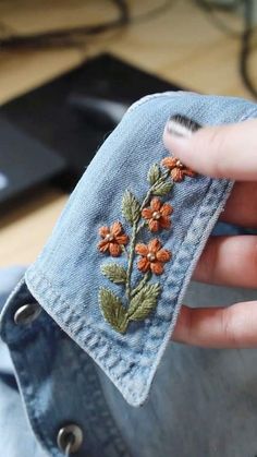 a woman's hand is holding an old pair of jeans with embroidered flowers on them