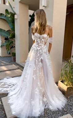 a woman wearing a white wedding dress with flowers on the skirt and off the shoulder