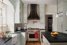 a kitchen with white cabinets and black counter tops, an oven hood over the stove