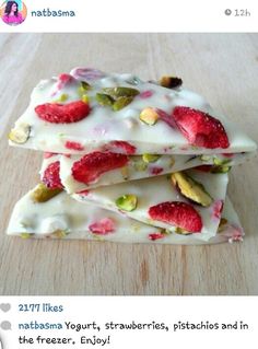 three pieces of white chocolate with strawberries and pistachios on top, sitting on a wooden surface