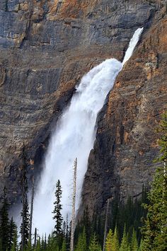 a large waterfall is coming out of the side of a mountain with trees around it