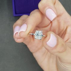 a woman's hand holding a diamond ring in front of her face with pink nail polish