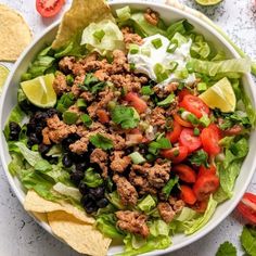 a bowl filled with lettuce, tomatoes and black beans next to tortilla chips