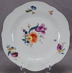 a white plate with colorful flowers painted on the front and sides, sitting on a stand