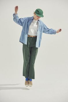 a person jumping in the air wearing a hat and green pants with their arms outstretched