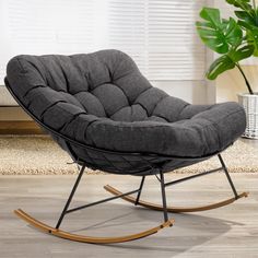 a grey rocking chair sitting on top of a wooden floor next to a potted plant