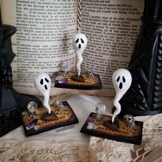 three halloween decorations sitting on top of a table next to an open book and candle