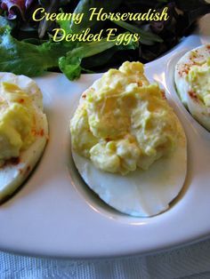 three deviled eggs on a white plate with greens