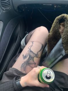 a person with tattoos on their legs sitting in the back seat of a car holding a can