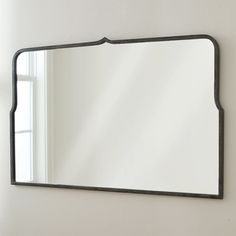 a mirror hanging on the wall in front of a window with white walls and windowsill