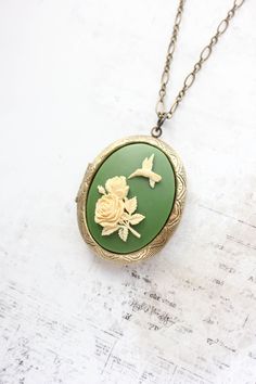 This is a gorgeous statement necklace with a big oval locket pendant in antique brass. The focal on the front of the locket is a resin cameo with an ivory cream humming bird and flower on a green background. This photo locket has beautiful details and will be a lovely accessory to store your treasured photos and mementos. This would be a beautiful gift for mom or anyone that loves romantic nature inspired accessories.  Details:  ~ The locket measures 1.5"w x 1.75 "h (36mm x 45mm) and has two ova Secret Hiding Spots, Nature Inspired Accessories, Romantic Nature, Hummingbird Necklace, Gold Locket Necklace, Bird And Flower, Oval Locket, Gold Locket, Frame Photo