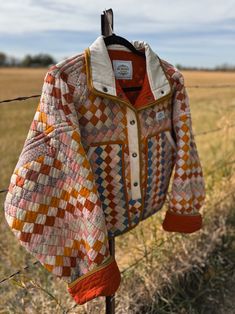 an orange and white jacket hanging on a wire fence in front of a grassy field