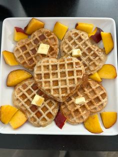 four waffles with butter and fruit arranged on a white square plate, ready to be eaten