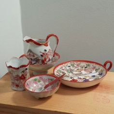 three pieces of pottery sitting on top of a wooden table next to a bowl and saucer