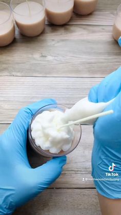 a person in blue gloves is holding a spoon with whipped cream on it and some cups behind them