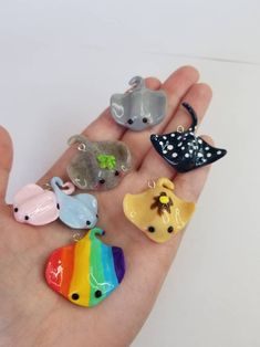 a person's hand is holding five small animal charms in different colors and shapes