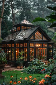 a glass house in the middle of some trees and flowers with lights on it's roof